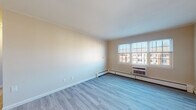 Located at 195 Admiral Kalbfus Rd in Newport, Rhode Island, this single-floor unit offers a clean, functional layout with a variety of updated finishes throughout. The living areas feature light-toned luxury vinyl plank flooring that enhances the sense of openness, while crown molding along the ceilings adds a refined architectural detail. Large multi-pane windows allow generous natural light to fill the main living space, offering views of the surrounding neighborhood. Baseboard heating and wall-mounted air conditioning units are present throughout, ensuring year-round comfort. The bedroom is finished with plush carpeting and mirrors the same windowed design, providing a quiet, well-lit retreat. The kitchen is efficiently designed with warm wood cabinetry, dark granite countertops, tile flooring, and stainless steel appliances including a gas range, dishwasher, and built-in microwave. The bathroom continues the granite aesthetic with a vanity countertop complemented by white subway tile wainscoting, a tile floor, and a well-placed mirror. The overall ambiance of the unit is bright, neutral, and move-in ready, making it a practical and comfortable residence in the heart of Newport.