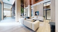 Located at 1114 Rue Saint-Antoine Ouest in the heart of downtown Montréal, this elegantly designed amenity space occupies a single, expansive floor that delivers an impressive sense of openness and volume. Soaring ceilings draw the eye upward to a dramatic, richly textured copper-finished ceiling feature that becomes the visual centerpiece of the main lounge area, casting a warm, reflective glow throughout the space.

Light ash wood flooring and matching wood-clad structural columns establish a cohesive palette of warm, natural tones, beautifully contrasted by a striking floor-to-ceiling marble accent wall in deep blue-grey, framing a sleek black steel shelving unit. Multiple seating vignettes furnished with crisp white and warm taupe sofas create distinct social zones within the open-plan layout, complemented by a large communal work table that accommodates collaborative use.

A separate media lounge area features a large-format television, comfortable sectional seating, and a dining arrangement with deep burgundy accent chairs, ideal for both casual gatherings and private screenings. Floor-to-ceiling black-framed glass partitions enclose a private meeting room outfitted with a round table and ergonomic seating, maintaining visual connectivity while offering acoustic separation. A mature indoor tree adds a touch of organic vitality, reinforcing the space's refined yet welcoming ambiance.