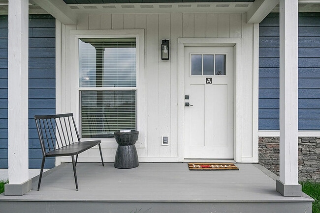 Inviting porch of a charming home featuring a white front door with a welcoming doormat, complemented by a stylish black bench and a modern side table. - Grace Lane Apartments