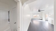 This efficiently designed 2-bedroom, 1-bathroom residence is laid out across a single floor, offering a practical and functional floor plan. The interior is finished with dark hardwood flooring throughout, contrasting cleanly against bright white walls that lend a crisp, airy feel to every room.

The main living area is a standout, featuring a decorative fireplace mantle painted white that serves as a focal point, complemented by a modern black ceiling fan overhead. Natural light filters in through a large window offering views of the neighboring brick architecture, adding character to the space.

The kitchen is thoughtfully appointed with white cabinetry, dark granite-style countertops, a stainless steel sink, and a bold black subway tile backsplash that adds a contemporary contrast. A stainless steel refrigerator completes the space.

The spacious primary bedroom benefits from its own ceiling fan and generous natural light. Both bedrooms are served by two closets, one of which features a walk-in configuration with built-in hanging rods. A connecting hallway provides smooth flow between rooms.

The full bathroom is finished in white tile, featuring a tub/shower combination, a vanity with sink, and dark hardwood-style flooring. Overall, the residence presents a clean, neutral aesthetic with functional, well-maintained finishes throughout.