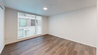 Located in Seattle's vibrant Fremont neighborhood, this one-bedroom, one-bathroom unit offers a thoughtfully designed layout with a clean, modern aesthetic throughout. The space is organized across a single floor, beginning with a sleek entrance hallway finished with dark hardwood-style flooring and recessed lighting that guides you into the main living areas.

The combined kitchen and living room serves as the heart of the unit, featuring warm hardwood-style floors, crisp white walls, and recessed lighting. The kitchen includes light wood cabinetry and stainless steel appliances, while the living area benefits from large floor-to-ceiling windows that invite natural light and provide views of the surrounding building exterior.

The bedroom is a comfortable retreat finished with plush wall-to-wall carpeting and its own large window, filling the room with natural light. A built-in wardrobe with wood-toned doors provides ample storage, and a wall-mounted heating unit ensures year-round comfort.

The bathroom is finished in a clean, contemporary style with a full soaking tub and shower combo, a vanity featuring light wood cabinetry with a modern sink, a large mirror, and hardwood-style flooring that ties the space together cohesively.

Overall, this unit offers a minimalist, modern design with functional finishes and abundant natural light throughout.