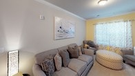This single-floor residence offers a thoughtfully designed layout with multiple bedrooms, two full bathrooms, a kitchen, and a living area. The living room features crown molding, neutral walls, and carpet flooring, creating a welcoming atmosphere with ample space for seating.

The kitchen is equipped with stainless steel appliances, including a refrigerator, range, and microwave. Dark espresso cabinetry is paired with granite-style countertops and wood-look plank flooring, providing a sleek, functional workspace.

The primary bedroom showcases a distinctive blue accent wall, dark hardwood furniture, and carpet flooring, with a ceiling fan overhead. A secondary bedroom maintains a lighter, neutral palette with natural light admitted through a window dressed with sheer yellow curtains.

Both bathrooms follow a consistent design language, featuring dark vanity cabinetry, white countertops, large mirrors, and a tub-shower combination. One bathroom includes wood-look plank flooring, while the other is finished with similar neutral tones.

Throughout the residence, a cohesive color scheme of warm grays and neutral tones ties the spaces together, while consistent use of dark-finished furniture and fixtures adds a refined contrast to the lighter walls and ceilings.