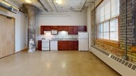 Located at 200 10th Street East in Saint Paul, MN, this one-bedroom, one-bathroom unit showcases the charm of industrial loft-style living within a converted historic building. The open-concept main area seamlessly combines the living room, dining space, and kitchen into one expansive, light-filled room. Polished concrete floors run throughout, complemented by exposed brick walls, original masonry columns, and overhead ductwork that lend a raw, authentic character to the space. Large windows with wood trim invite ample natural light and feature baseboard heating beneath them. The kitchen is well-appointed with rich cherry wood cabinetry, full-length upper and lower cabinets, a full suite of white appliances including a stove, dishwasher, microwave, and refrigerator, and a double-basin sink with gray countertops. The bedroom offers a comfortable layout with a ceiling fan, a natural-light window, and access to two closets for generous storage. The bathroom features soft blue walls, a wood-toned vanity with a wide mirror, and a large, well-lit countertop. Two closets provide additional organization throughout the unit. This space delivers an urban, industrial aesthetic with practical conveniences in the heart of Saint Paul.