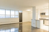 Located on the fourth floor at 1465 Lawrence Ave W in Toronto, this two-bedroom, one-bathroom unit offers a well-organized and functional layout across a single floor. Polished parquet flooring runs throughout the unit, lending warmth and a classic character to every room.

The open-concept living room is generously proportioned, featuring large windows fitted with baseboard heating units that allow natural light to fill the space while offering views of the surrounding greenery and neighbourhood. A mirrored sliding closet door near the entryway adds a reflective element that enhances the sense of openness.

The kitchen is efficiently designed with white cabinetry, a patterned tile backsplash, and stainless steel appliances including a range and over-the-range microwave. A peninsula counter with a dark surface connects the kitchen to the living area, creating a practical divide while maintaining visual flow.

The primary bedroom is well-sized and bright, with a window overlooking an open outdoor area. The second bedroom is also a comfortable size with its own window and baseboard heating. Both rooms share clean white walls and parquet flooring consistent with the rest of the unit.

The bathroom features a full soaker tub and shower combination, finished with classic white subway tiles and chrome fixtures, giving it a clean, timeless aesthetic. A hallway connects all rooms, providing a clear and practical circulation path throughout the unit.