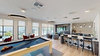 Located at 651 East 6th Street in Tempe, Arizona, this thoughtfully designed amenity space offers a well-rounded mix of social, recreational, and professional environments across a single floor. Light wood flooring and crisp white walls create a clean, contemporary foundation throughout.

The main lounge and social area serves as the centerpiece, anchored by a pool table and a striking dark mosaic tile feature wall with a gold-framed flat-screen TV. Circular pendant lighting adds warmth overhead, while a wet bar kitchenette with mosaic tile backsplash, under-counter appliances, and a sink provides convenient refreshment options nearby.

A long marble-topped communal bar with high-back chairs offers a co-working or casual dining setting, illuminated by a sleek multi-bulb pendant fixture. Curated artwork lines the walls, enhancing the polished aesthetic. Along the perimeter, floor-to-ceiling windows flood the space with abundant natural light and frame views of the surrounding Tempe streetscape, including palm trees and distant mountain ridgelines.

Cozy lounge seating with swivel chairs and a low coffee table creates an inviting social nook, while small café-style tables with terracotta chairs line the window wall for intimate gatherings. A separate private conference room features a large wood table, upholstered chairs, a wall-mounted display, textured accent wallpaper, and a statement pendant light — ideal for focused meetings.