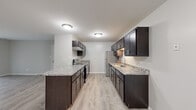 Located at 951 Golf Course Rd in Crystal Lake, IL, this single-floor, two-bedroom, one-bathroom home offers a well-organized and functional layout. The living room is bright and open, featuring wood-look luxury vinyl flooring and a large sliding glass door with vertical blinds that fills the space with natural light. The kitchen is a standout feature, designed in a galley style with rich dark cabinetry, granite-patterned countertops, stainless steel appliances including a refrigerator and electric range, and a central island that adds both prep space and visual appeal. Light wood-look flooring continues throughout the kitchen, complementing the contemporary aesthetic. Both bedrooms are carpeted and offer a comfortable, quiet atmosphere. The primary bedroom is generously sized and includes direct access to a dedicated walk-in closet outfitted with shelving and hanging rods. The shared bathroom features a tub-shower combination and open built-in shelving for additional storage. A dedicated in-unit laundry room includes a full-size washer and dryer with overhead wire shelving. Neutral gray tones throughout the home create a clean, cohesive look ideal for a variety of décor styles.