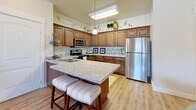 Located in Midvale, Utah, this single-floor, 2-bedroom, 2-bathroom residence offers a thoughtfully designed layout with warm, neutral tones and quality finishes throughout. The open-concept kitchen is a standout feature, boasting rich wood cabinetry, granite countertops, stainless steel appliances, and a central island with seating — ideal for both cooking and casual dining. The kitchen flows naturally into the combined living and dining area, where hardwood-style flooring, a ceiling fan, and large windows invite an abundance of natural light and views of the surrounding neighborhood. The spacious primary bedroom features plush carpet, multiple windows with neighborhood views, and generous closet space, while the second bedroom offers a similarly comfortable and well-lit retreat. Both bathrooms are cleanly finished, with one featuring a tub-shower combination, wood-toned vanity cabinetry, and dark granite countertops paired with light hardwood-style flooring. A dedicated in-unit laundry area adds everyday convenience. With four closets distributed throughout, storage is plentiful. The overall ambiance is warm and inviting, combining functional design with tasteful, contemporary styling suited for comfortable living.