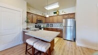 Located in Midvale, Utah, this single-floor, 2-bedroom, 2-bathroom residence offers a thoughtfully designed layout with warm, neutral tones and quality finishes throughout. The open-concept kitchen is a standout feature, boasting rich wood cabinetry, granite countertops, stainless steel appliances, and a central island with seating — ideal for both cooking and casual dining. The kitchen flows naturally into the combined living and dining area, where hardwood-style flooring, a ceiling fan, and large windows invite an abundance of natural light and views of the surrounding neighborhood. The spacious primary bedroom features plush carpet, multiple windows with neighborhood views, and generous closet space, while the second bedroom offers a similarly comfortable and well-lit retreat. Both bathrooms are cleanly finished, with one featuring a tub-shower combination, wood-toned vanity cabinetry, and dark granite countertops paired with light hardwood-style flooring. A dedicated in-unit laundry area adds everyday convenience. With four closets distributed throughout, storage is plentiful. The overall ambiance is warm and inviting, combining functional design with tasteful, contemporary styling suited for comfortable living.