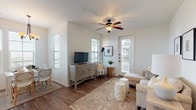 This single-story residence is thoughtfully designed with a cohesive, neutral palette and warm wood-look flooring that flows through the main living areas. The living room is an inviting, well-lit space featuring a ceiling fan, multiple windows with slatted blinds that allow generous natural light, and direct access to an exterior door. Framed artwork and understated furnishings contribute to a relaxed, coastal-inspired atmosphere.

Adjacent to the living area, the dining space accommodates a full dining table beneath an elegant chandelier, flanked by large windows that bring in abundant natural light. The kitchen is well-appointed with rich, dark wood cabinetry, granite-style countertops, and a full suite of stainless steel appliances, including a refrigerator, electric range, and over-the-range microwave.

The bedrooms feature plush carpeting and ceiling fans, offering a comfortable retreat. The primary bedroom includes access to a walk-in closet. The bathroom is finished with dark-framed cabinetry, granite countertops, wood-look flooring, and a tiled tub-shower combination.

A dedicated laundry area houses a full-size washer and dryer with overhead shelving, adding practical convenience to this well-rounded residence.