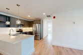 Located at 128 Maple Street in Danvers, MA, this thoughtfully designed 2-bedroom, 1-bathroom unit offers a clean, modern aesthetic throughout. The open-concept kitchen and living area serves as the heart of the home, showcasing a stunning quartz waterfall island with an undermount sink, stylish globe pendant lighting, and dark two-tone cabinetry paired with a marble-look tile backsplash. Stainless steel appliances, including a French door refrigerator, range, and microwave, complete the well-appointed kitchen. Light-toned hardwood-style flooring flows seamlessly throughout the entire unit, enhancing the bright, airy feel. The living area extends naturally from the kitchen, bathed in natural light from multiple windows with views of the surrounding neighborhood. Both bedrooms are comfortably sized, each featuring sliding closet doors with built-in shelving and large windows that invite abundant natural light. The full bathroom is finished with large-format tile flooring, a dark vanity with a white quartz countertop, a lighted mirror, brushed gold fixtures, and a full soaking tub with shower. Recessed lighting and crisp white walls throughout lend a fresh, move-in-ready appeal to this well-designed Danvers residence.