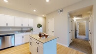This single-floor, 3-bedroom, 2-bathroom residence offers a thoughtfully planned layout with a clean, contemporary aesthetic. The combined kitchen and living area serves as the heart of the home, featuring light hardwood-style flooring, recessed lighting, and a neutral warm-beige color palette. The kitchen is well-appointed with white shaker-style cabinetry, stainless steel appliances including a refrigerator, gas range, and microwave, complemented by a central island with a quartz-style countertop that provides additional prep and dining space.

The three bedrooms are carpeted for comfort, with the primary bedroom offering generous proportions, a ceiling fan, a window for natural light, and access to a dedicated closet outfitted with wire shelving systems that maximize storage capacity. The additional bedrooms maintain the same neutral tones and soft carpet flooring.

The two bathrooms are finished in a modern, minimalist style. One features a walk-in glass-door shower with chrome fixtures and light tile flooring. The second bathroom includes a single vanity with under-cabinet storage, a mirror, and coordinating light fixtures. A hallway connects the bedrooms and bathrooms, maintaining a clean flow throughout the home. Overall, the space presents a fresh, move-in-ready feel with consistent finishes across all rooms.