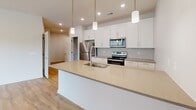 This well-appointed 2-bedroom, 2-bathroom single-floor residence offers a thoughtfully designed layout with modern finishes throughout. The open-concept kitchen serves as a central highlight, featuring crisp white shaker cabinetry, a subway tile backsplash, stainless steel appliances including a refrigerator, range, and microwave, and a generous quartz-topped island with a built-in sink and pendant lighting overhead. Light hardwood-style flooring flows through the main living areas, complementing the neutral color palette. The spacious living room is filled with natural light from large windows and a sliding glass door that opens to an outdoor balcony, with recessed lighting providing additional illumination. Both bedrooms are carpeted and include ceiling fans and windows with roller shades. The primary bedroom is a comfortable size and is supported by ample closet space, including double panel doors leading to well-organized closets. The bathrooms are finished with wood-look flooring, vanities with undermount sinks, and a glass-enclosed walk-in shower with built-in shelving. A dedicated hallway laundry area accommodates a stacked washer and dryer. Three closets throughout the unit provide generous storage, with wire shelving systems for organization.