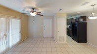 This single-story residence offers a straightforward, functional layout with distinct zones for living, sleeping, cooking, and bathing. The galley-style kitchen is efficiently arranged with dark espresso cabinetry lining both sides, granite-look countertops, a double stainless steel sink, black appliances including an electric range and over-the-range microwave, and light tile flooring that extends throughout the main living areas.

The open living and dining area is finished with the same light tile flooring and features a ceiling fan with an integrated light fixture, neutral beige walls, and direct access to the front entry door. A closet adjacent to the entryway provides convenient storage. The space connects seamlessly to the kitchen, supporting an open and practical flow.

The bedroom is carpeted in a warm brown tone, offering a softer, more comfortable feel underfoot. A ceiling fan with lighting is also present here, and a window with blinds allows natural light into the room.

The bathroom includes a full tub and shower combination with white tile surround, a curved shower rod, dark cabinetry overhead for storage, and light tile flooring. Overall, the unit maintains a cohesive, neutral palette with consistent dark cabinetry accents and ceiling fans throughout.