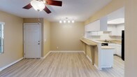 This single-floor space offers a practical and cohesive layout that connects its main living areas seamlessly. Consistent wood-style flooring runs throughout, lending a unified and clean aesthetic to the entire unit. Warm neutral-toned walls complement the light flooring and contribute to a bright, welcoming ambiance across all rooms.

The kitchen is efficiently designed with white cabinetry providing ample storage, light-toned countertops, and a full suite of black appliances, including a range, dishwasher, and refrigerator. A peninsula counter with an overhang connects the kitchen to the adjacent dining area, creating a natural transition between spaces and offering casual seating potential.

The dining area benefits from a track lighting fixture and a ceiling fan, while an entry door anchors one end of the space. The living areas feature additional ceiling fans with light kits and textured ceilings throughout.

A generously sized room with sliding glass doors opens to an outdoor area, allowing natural light to fill the space. This room also includes a louvered closet door revealing built-in shelving. An additional room features a large window with vertical blinds, offering ample natural light and a ceiling fan overhead.