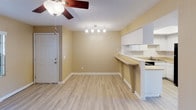 This single-floor space offers a practical and cohesive layout that connects its main living areas seamlessly. Consistent wood-style flooring runs throughout, lending a unified and clean aesthetic to the entire unit. Warm neutral-toned walls complement the light flooring and contribute to a bright, welcoming ambiance across all rooms.

The kitchen is efficiently designed with white cabinetry providing ample storage, light-toned countertops, and a full suite of black appliances, including a range, dishwasher, and refrigerator. A peninsula counter with an overhang connects the kitchen to the adjacent dining area, creating a natural transition between spaces and offering casual seating potential.

The dining area benefits from a track lighting fixture and a ceiling fan, while an entry door anchors one end of the space. The living areas feature additional ceiling fans with light kits and textured ceilings throughout.

A generously sized room with sliding glass doors opens to an outdoor area, allowing natural light to fill the space. This room also includes a louvered closet door revealing built-in shelving. An additional room features a large window with vertical blinds, offering ample natural light and a ceiling fan overhead.