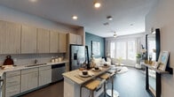 This well-designed single-floor residence offers a thoughtful layout that seamlessly blends style and functionality. The open-concept kitchen and living area serves as the heart of the home, where light wood cabinetry, granite countertops, and a full suite of stainless steel appliances — including a French door refrigerator, dishwasher, microwave, and range — create a polished, modern kitchen. A central island with bar seating provides additional dining and prep space. The living area flows naturally from the kitchen, anchored by a bold slate-toned accent wall, large windows with abundant natural light, and a ceiling fan that enhances the airy atmosphere. The primary bedroom features neutral tones, dark hardwood-style flooring, and a window that brings in soft natural light, while a second bedroom is distinguished by a striking blue accent wall and framed urban artwork, lending it a dynamic, artistic character. The bathroom is designed with a long, functional layout, offering a double-sink granite vanity, modern cabinetry, large-format tile flooring, and a full bathtub with a tiled surround. Dark hardwood-style flooring runs consistently throughout the main living areas, tying the space together with a warm yet contemporary feel.