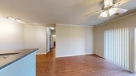 This one-bedroom, one-bathroom unit at 5210 Bagby Ave in Waco, Texas offers a well-organized, efficient layout across a single floor. The open living area is finished with warm wood-look flooring, crown molding, and a ceiling fan, creating a clean and comfortable atmosphere. Natural light flows in through a sliding glass door that leads to an outdoor patio, complemented by vertical blinds for privacy. The kitchen runs along a galley-style corridor featuring medium-toned wood cabinetry, dark granite-style countertops, black appliances including a range, microwave, and refrigerator, as well as a double sink with a modern faucet. Track lighting overhead keeps the space well-lit and functional. The bedroom is carpeted for added comfort and includes a ceiling fan, a window with outdoor views, and a closet with a six-panel door. The full bathroom features a tub-shower combination with tile surround accented by a diamond pattern, wood-look flooring, a wood vanity with countertop, and a medicine cabinet mirror. A dedicated laundry area houses a full-size washer and dryer with wire shelving above for additional storage. Crown molding throughout the living areas adds a refined finishing touch to this practical and comfortable unit.