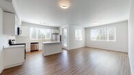 This single-floor residence is designed with a clean, contemporary aesthetic and a practical layout that maximizes both comfort and functionality. The open-concept living and kitchen area serves as the heart of the home, bathed in natural light through multiple large windows with views of surrounding evergreen trees. Wood-style flooring runs throughout the main living spaces, lending warmth and continuity to the design.

The kitchen is well-appointed with white shaker-style cabinetry extending to the ceiling for ample storage, light-colored quartz countertops, and a full suite of stainless steel appliances including a range, microwave, dishwasher, and refrigerator. A central island provides additional prep space and casual seating. The kitchen flows seamlessly into the spacious living area, making the space well-suited for everyday living and entertaining.

The bedrooms are carpeted for comfort and feature windows that frame natural wooded views. Each bedroom connects to a bathroom finished with white cabinetry, quartz countertops, a single-basin sink, a large mirror, and wood-style flooring. The hallways are clean and uncluttered, contributing to the home's overall sense of openness. Neutral tones and modern hardware finishes tie the entire space together cohesively.