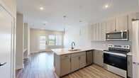 Located in Spring, TX, this well-appointed one-bedroom, one-bathroom unit offers a modern and cohesive design across its single floor. The open-concept kitchen is a standout feature, showcasing a peninsula with a white quartz countertop and an integrated sink, complemented by two-tone cabinetry — light wood uppers paired with matte gray lower cabinets. A full suite of stainless steel appliances, including a refrigerator, range, and over-the-range microwave, adds a polished, contemporary feel. Pendant lighting and recessed ceiling lights illuminate the space effectively. Light wood-look vinyl plank flooring flows consistently throughout the living areas and bedroom, lending warmth and visual continuity. The bedroom is generously sized with a large window that invites natural light and provides open outdoor views, while a ceiling fan ensures year-round comfort. Built-in open shelving in the bedroom provides convenient display or storage space. The walk-in closet is well-organized with dual hanging rods and shelving across multiple walls. The bathroom features large-format marble-look tile flooring, a sleek vanity with white countertops, dark hardware accents, and direct access to the walk-in closet, creating a practical and elegant private suite.