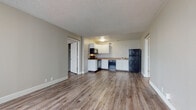 Located at 3129 Sinton Rd in Colorado Springs, Colorado, this single-floor unit offers a clean, functional layout designed for comfortable everyday living. The open-concept main area seamlessly connects the living space to the kitchen, both finished with warm wood-style vinyl plank flooring that extends throughout most of the unit. The kitchen is well-equipped with white shaker-style cabinetry, stone-patterned countertops, and a full suite of black appliances including a range, over-the-range microwave, dishwasher, and refrigerator — providing ample functionality for home cooking. A stainless steel sink is positioned beneath a window, adding a touch of natural light to the workspace. The bedroom features a large window with vertical blinds that invites generous natural light and provides outdoor views, along with a closet and direct access to the bathroom vanity area. The bathroom includes a full tub-shower combo with white tile surround, a toilet, and light tile flooring, maintaining a bright and clean aesthetic. A textured ceiling runs throughout the unit, adding subtle character. The layout, as seen in the dollhouse view, is compact yet efficient, with well-defined zones for living, sleeping, and bathing.