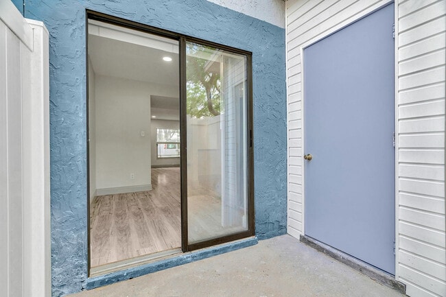 Inviting apartment entrance with modern sliding glass door opening to bright, spacious interior featuring elegant wood flooring. - Temple Crest Townhomes