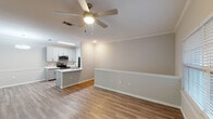 This upper-floor residence in Mobile, AL offers a well-designed two-bedroom, two-bathroom layout accessed via a carpeted staircase. The open-concept living and dining area features warm wood-look flooring, crown molding, and a ceiling fan with light fixture, creating a bright and functional common space. The kitchen is outfitted with gray shaker-style cabinetry, white quartz countertops, a tile backsplash, and stainless steel appliances including a range, microwave, and refrigerator. A peninsula with an undermount sink adds additional workspace and casual dining potential. Both bedrooms feature plush carpeting, natural light from window blinds, ceiling fans, and walk-in or reach-in closets with wire shelving. Each bathroom includes a tub-shower combination with tiled surround, a single-sink vanity with white countertop, and wood-look flooring. Neutral tones and clean finishes are carried consistently throughout the unit, contributing to a cohesive and move-in-ready ambiance. Crown molding and white trim details add a polished touch to the overall interior aesthetic.