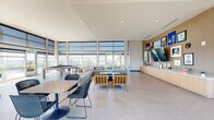 Located at 480 N Terry Ave in Orlando, Florida, this elevated amenity lounge spans a generous footprint and delivers a polished, modern aesthetic designed for both social gatherings and relaxed everyday use. Floor-to-ceiling curtain-wall windows wrap the interior, flooding the space with abundant natural light and framing panoramic views of the downtown Orlando skyline and surrounding cityscape.

The main lounge area is thoughtfully arranged with modular sectional sofas, accent armchairs, and a variety of dining and lounge tables topped with woven chairs, creating distinct zones for conversation, dining, and recreation. A billiard table anchors one corner, adding a leisure element to the open-plan layout. One wall features a built-in light wood credenza topped with a large flat-screen television and a curated gallery of framed artwork, lending a residential warmth to the contemporary design. Large-format porcelain tile flooring runs throughout, reinforcing the clean, cohesive aesthetic.

A kitchenette area provides a sink, refrigerator, and light wood cabinetry with open shelving, making the space fully functional for events and gatherings. Lush indoor plants add organic texture throughout.

Extending beyond the glass doors, a wide outdoor terrace runs the full length of the building, fitted with bar-height seating and glass-panel railings that preserve unobstructed views of the Orlando skyline — an exceptional setting for enjoying Florida's sunny climate.