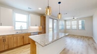 This thoughtfully designed single-floor residence showcases a clean, contemporary aesthetic with a cohesive palette of light tones and quality finishes throughout. The heart of the home is an open-concept kitchen that flows seamlessly into the living area, featuring a large central island topped with granite countertops, a two-tone cabinetry scheme combining warm wood and crisp white, stainless steel appliances, and stylish amber pendant lights. Multiple windows and a glass door flood the space with natural light, complemented by light hardwood flooring underfoot. The bedrooms offer a calm retreat, with soft carpeted flooring, ceiling fans, and windows that invite in daylight and exterior views. A bright hallway with recessed lighting and hardwood floors connects the living areas to the private spaces. The bathrooms are well-appointed, with one featuring a long white vanity with modern hardware, a large mirror, and a tiled shower, while another includes a soaking tub with tiled surround and direct access to a walk-in closet complete with built-in shelving and hanging rods. Throughout the home, clean white walls, wide baseboards, and consistent finishes create a polished, move-in-ready atmosphere.
