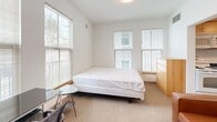 Located at 115 S Quarry St in Ithaca, NY, this two-bedroom, one-bathroom unit offers a thoughtfully arranged single-floor layout that maximizes every square foot. The open living area serves as the heart of the home, featuring neutral-toned walls and a cozy atmosphere suited for both relaxing and entertaining. The kitchen is efficiently designed with light maple cabinetry, dark granite countertops, tile flooring, and full-size appliances including a top-freezer refrigerator, providing practical functionality in a compact footprint. The generously sized primary bedroom stands out with multiple windows that invite abundant natural light and outdoor views, complemented by soft carpeting for added comfort. The second bedroom also features carpeted flooring, a large double-door closet with frosted panel doors, a window with blinds, and ample space for a desk and seating area, making it well-suited as either a guest room or a home office. The shared bathroom includes a full tub and shower combination with a curtain rod, tile flooring, and clean, minimalist finishes. Throughout the unit, the consistent use of white walls, tile and carpet flooring, and brushed chrome hardware creates a cohesive, modern aesthetic.
