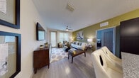 Located at 3603 Pavilion Palms Circle in Riverview, Florida, this single-floor residence showcases a contemporary design with a cohesive color palette of olive green, cool gray, and warm neutrals throughout. The open living area features wood-style plank flooring, a ceiling fan, and large windows fitted with blinds that invite abundant natural light. A bold olive green accent wall anchors the living space, complemented by tasteful wall art and stylish furnishings. The kitchen is outfitted with espresso-toned cabinetry, granite countertops, a classic subway tile backsplash, and a full suite of stainless steel appliances, including a range, microwave, dishwasher, and refrigerator. Multiple bedrooms offer plush carpeting, ceiling fans, generous windows, and distinctive accent walls in soothing hues of olive and slate blue. The bathrooms are well-appointed, featuring large-format tile flooring, dark espresso vanity cabinetry, granite countertops, and illuminated mirrors. One bathroom includes a soaking tub with marble-style tile surround, while another provides a dual-sink vanity with ample storage. Together, the rooms reflect a thoughtfully designed living space that balances modern aesthetics with everyday functionality.