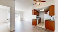 This single-floor unit offers a practical and well-organized layout that seamlessly connects the main living areas. The open-plan living and dining area is finished with light wood-style flooring and is served by a ceiling fan with integrated lighting. A wall-mounted heater unit provides supplemental warmth, and a sliding glass door floods the space with natural light while providing direct access to an outdoor area.

The kitchen is positioned adjacent to the living space in a compact galley-style configuration. It features warm medium-toned wood cabinetry extending to the upper and lower walls, granite-style countertops, a double sink, and white appliances including a gas range, refrigerator, and dishwasher. A skylight-style ceiling fixture adds overhead illumination to the cooking area, which is finished with neutral tile flooring.

The bedroom is carpeted and benefits from natural light through a vertical-blind-covered window. It includes a built-in closet with mirrored sliding doors framed in gold-tone hardware, offering practical storage.

The bathroom features tile flooring, a wood-toned vanity with a white countertop and single sink, a large mirror, a medicine cabinet, and a four-bulb vanity light above. The textured ceilings are consistent throughout, contributing to the unit's cohesive, clean aesthetic.