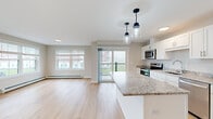 Located at 28 Hackamore in Scarborough, Maine, this single-floor residence offers a clean, modern design with an open-concept living and kitchen area that maximizes both functionality and flow. Light hardwood flooring runs throughout the main living spaces, complementing the neutral, warm-toned walls and crisp white trim.

The kitchen is a standout feature, equipped with white shaker-style cabinetry, granite countertops, a central island with additional seating and storage, stainless steel appliances — including a refrigerator, range, microwave, and dishwasher — and a stainless undermount sink. Stylish pendant lighting above the island adds a contemporary touch. A sliding glass door leads from the living area to a private balcony, while large windows invite abundant natural light and views of the surrounding community.

The bedrooms are carpeted for comfort and each features windows with blinds, baseboard heating, and generous closet space. A dedicated storage or utility area with hardwood flooring adds practical value. Additional climate control is provided by a wall-mounted mini-split unit. The overall aesthetic is bright, clean, and move-in ready, reflecting thoughtful, modern construction suited for comfortable everyday living in the Scarborough community.