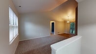 This single-floor home showcases a thoughtfully designed open layout that maximizes both space and functionality. The living area is a standout feature, boasting dramatic vaulted ceilings that create an expansive, airy atmosphere. Plush wall-to-wall carpeting adds warmth underfoot, while a large sliding glass door allows natural light to pour in and offers views of the surrounding greenery. A pendant light fixture above the adjacent dining area provides a welcoming focal point, and the transition between the living and dining spaces flows naturally.

The kitchen is well-appointed with rich medium-toned wood cabinetry, dark granite-style countertops, and durable wood-look flooring. Stainless steel appliances — including a dishwasher, range, and microwave — complement the cabinetry, while a window above the sink brings in additional natural light.

An interior pass-through window connects the kitchen to the living area, enhancing the open, communicative feel of the floor plan. The bedroom is generously sized with soft carpeting and a window overlooking mature trees outside. The bathroom features a full tub-shower combination with clean white tile surround, stone-look tile flooring, granite-topped vanity, and a bright window fitted with blinds for privacy.