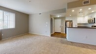 This single-floor residence offers a thoughtfully designed layout that balances comfort and functionality. The open-concept living area is finished with neutral-toned carpet and warm gray walls, creating a welcoming atmosphere. Track lighting and recessed fixtures illuminate the space effectively, while an arched entryway connects the living area to the foyer, which features wood-look flooring that extends into the kitchen.

The kitchen is well-equipped with crisp white cabinetry, dark granite-style countertops, and a full suite of stainless steel appliances including a gas range, microwave, and dishwasher. A breakfast bar adds casual dining flexibility.

The unit includes two bedrooms, each carpeted and fitted with ceiling fans for year-round comfort. The primary bedroom features a walk-in closet, a private en-suite bathroom with a shower/tub combination and sliding glass enclosure, and a sliding glass door that opens to a private balcony with views of the surrounding landscape. The second bedroom benefits from natural light through double windows. A second full bathroom serves the remaining living areas, also featuring a tub/shower combination, wood-look flooring, and dark countertop vanity with ample mirror space.