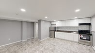 Located at 314 E 24th St in Chester, PA, this thoughtfully designed single-floor unit offers a clean, modern aesthetic throughout. Marble-look porcelain tile flooring spans the entire space, lending a cohesive and polished look from the entry corridor through every room.

The kitchen is a standout feature, outfitted with crisp white shaker-style cabinetry extending to the ceiling for generous storage capacity. Dark granite countertops provide striking contrast against the white cabinetry, while a mosaic glass tile backsplash adds a refined decorative touch. Stainless steel appliances — including a refrigerator, electric range, and under-cabinet range hood — complete the functional and stylish kitchen setup. Recessed lighting illuminates the space efficiently throughout.

An open main living area offers a versatile, light-filled space with neutral gray walls, white baseboards, and recessed ceiling lights. A paneled white door leads to additional utility access, and an electrical panel is neatly integrated into the wall.

The bathroom is well-appointed with a full tub and shower surround in crisp white, accompanied by a toilet and a white vanity with sink. Recessed lighting and the same marble-look tile flooring maintain visual continuity with the rest of the unit.

A narrow corridor connects the rooms, reinforcing the efficient, well-organized layout of this neatly renovated space.