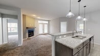 This well-appointed single-story home offers four bedrooms, two full bathrooms, and a thoughtfully designed layout that maximizes comfort and functionality. The open-concept kitchen and living room serve as the heart of the home, highlighted by a granite-topped breakfast bar peninsula with pendant lighting overhead and a ceiling fan that anchors the living space. The kitchen is outfitted with rich dark-espresso cabinetry, granite countertops, stainless steel appliances including a refrigerator, electric range, and microwave, and light wood-look flooring. The living room features plush carpet, neutral gray walls, and a corner gas fireplace with a granite hearth and wood mantel, complemented by French doors that invite natural light. A carpeted hallway connects the bedrooms and common areas seamlessly. The primary bedroom is generously sized and includes a walk-in closet equipped with wire shelving systems for organized storage. Both bathrooms are finished with light tile flooring and gray tile tub/shower surrounds—one featuring a soaking tub and the other a walk-in shower with sliding glass doors and dark vanity cabinetry. Additional highlights include a dedicated utility room and multiple closets throughout.