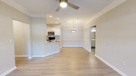 This single-story residence offers a well-designed open-concept layout that seamlessly connects the main living areas. The living room is anchored by a ceiling fan and access to an outdoor balcony through a glass-paneled door flanked by windows, filling the space with natural light. Crown molding and light hardwood-style flooring run throughout the main living areas, contributing to a clean, cohesive aesthetic.

The kitchen is thoughtfully appointed with white cabinetry, granite-style countertops, a tile backsplash, and stainless steel appliances including a built-in microwave, electric range, and refrigerator. A raised breakfast bar provides a casual dining option while maintaining the open flow.

A dedicated dining area adjoins the kitchen and living space, distinguished by decorative wainscoting panels along the lower walls and pendant lighting overhead, lending a touch of classic character.

The bedrooms feature plush carpeting, ceiling fans, and closet access, offering a comfortable retreat. The bathroom includes a granite-topped vanity, wood-style flooring, and a shower-tub combination. Throughout the unit, neutral tones and consistent finishes create a bright, welcoming atmosphere.