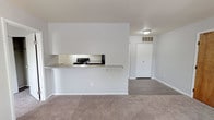 Located at 507 S Main St in Englewood, Ohio, this single-floor unit offers a clean, functional layout with a neutral color palette throughout. The open-concept living area features wall-to-wall carpet and is anchored by a pass-through kitchen counter that connects the living space to the kitchen. The kitchen is equipped with dark cabinetry, a laminate countertop with a subtle marble-like finish, and a black electric range, all set atop durable hardwood-style flooring. A passthrough window with an extended countertop bar provides a casual dining or prep area while maintaining an open connection to the living room. The living room receives natural light through a window fitted with blinds and includes a wood-toned entry door that adds warmth to the otherwise crisp, white interior. A hallway leads to the bedroom, which is generously proportioned with plush carpeting and a window overlooking the outdoors. The bathroom features a wide white vanity with ample drawer storage, a well-lit mirror with a bar-style light fixture, and a separate enclosed bathing area. A closet is conveniently positioned in the hallway just outside the bathroom, offering practical storage. The overall ambiance is bright, clean, and move-in ready.