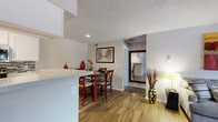 This single-floor residence offers a cohesive, functional layout with consistent design details throughout. The living room serves as a central gathering space, anchored by a white brick fireplace with a classic mantel and built-in shelving on one side. Wood-look flooring runs through the main living areas, complementing the neutral gray walls and textured ceilings. Multiple windows allow natural light to filter into the space, with a glass-paned door providing additional brightness and outdoor access.

The dining area connects seamlessly to the kitchen and living space, accommodating a round dining table with comfortable seating. The kitchen is efficiently designed, featuring white cabinetry, granite-style countertops, a tile backsplash, and a full suite of stainless steel appliances including a refrigerator, range, and microwave. A peninsula counter provides a natural division between the kitchen and dining space.

The bedroom is generously proportioned, featuring plush carpeting, a ceiling fan, and multiple windows that invite outdoor views. The bathroom includes white cabinetry with updated hardware and granite-style countertops. Overall, the space maintains a clean, move-in-ready aesthetic with practical finishes throughout.