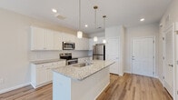 This single-floor residence offers a thoughtfully designed open-concept layout that seamlessly connects the kitchen, dining, and living areas. The kitchen is a standout feature, showcasing crisp white shaker-style cabinetry, a classic subway tile backsplash, and a generous granite-topped island with an undermount sink. Stainless steel appliances — including a range, microwave, and refrigerator — complement the bright, clean aesthetic, while elegant pendant lights suspended above the island add a refined finishing touch. Light wood-look flooring runs throughout the main living areas, enhancing the airy, cohesive feel of the space. The living area is bathed in natural light, courtesy of a sliding glass door that opens to an outdoor view and is complemented by a ceiling fan overhead. The bedroom features plush carpeting, a ceiling fan, and a bright window that fills the room with natural light. The bathroom is finished with white cabinetry, a wide vanity with an undermount sink, a large mirror, and a shower-tub combination. A walk-in closet is accessible directly from the bathroom, adding practical storage. Throughout the residence, neutral tones and clean lines create a welcoming, move-in-ready atmosphere.