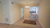This single-floor residence offers a practical and cohesive layout designed for comfortable everyday living. The dining area is highlighted by an elegant chandelier that anchors the space, casting warm light over the carpeted flooring below. A decorative area rug adds a touch of personality to the open room.

A defining architectural feature is the partial dividing wall that separates the dining area from the kitchen while maintaining a sense of openness between the two spaces. This thoughtful design allows for easy interaction between the rooms without fully closing them off from one another.

The kitchen is well-appointed with classic white cabinetry that extends to the upper walls, providing ample storage. A white electric range serves as the cooking centerpiece, complemented by a countertop that wraps along the perimeter. A window above the kitchen area allows natural light to filter in, brightening the workspace. A baseboard heating unit ensures year-round comfort throughout the space.

The walls throughout are finished in a warm, neutral tone that lends a clean and inviting ambiance, while a textured ceiling adds subtle character overhead. Ceiling-mounted ventilation and thoughtful outlet placements speak to the functional design of this well-maintained single-floor home.