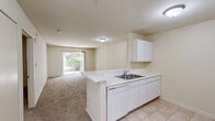 Located at 1420 Commons Dr in Woodstock, IL, this one-bedroom, one-bathroom unit offers a well-organized single-floor layout designed for comfortable everyday living. The space is thoughtfully arranged with a kitchen, hallway, bathroom, and bedroom, making efficient use of every square foot.

The kitchen features light tile flooring, white cabinetry, and includes a full-size refrigerator, providing a clean and functional cooking space. The neutral cream-toned walls and simple finishes create a bright, understated aesthetic throughout.

The bedroom is a comfortable, well-proportioned room finished with wall-to-wall carpeting that adds warmth underfoot. A window allows natural light to filter in, offering a pleasant view of the surrounding greenery. A closet door is also visible, providing convenient storage within the room.

The bathroom is outfitted with a full tub and shower combination, complete with a grab bar for added safety and a curtain rod. The tile flooring and crisp white surround give the bathroom a clean, practical feel.

A connecting hallway ties the rooms together, contributing to the unit's efficient flow. The overall ambiance is calm and neutral, offering a move-in-ready canvas well-suited for a range of personal styles.