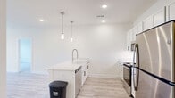 Located at 5 Views Lake Dr in Clayton, NC, this single-story, 2-bedroom, 3-bathroom home offers a clean, modern aesthetic with thoughtful design throughout. The open-concept living, dining, and kitchen area serves as the heart of the home, featuring light wood-look flooring, recessed lighting, and an abundance of natural light from large windows and a glass-panel entry door. The kitchen is a standout, showcasing white shaker cabinetry with matte black hardware, a subway tile backsplash, quartz countertops, a farmhouse-style sink, stainless steel appliances, and a central island with elegant pendant lighting overhead. The spacious primary bedroom includes plush carpeting, a ceiling fan, and a well-sized walk-in closet with wire shelving. The en-suite primary bathroom features light wood-look flooring, white vanity cabinetry, and a glass-enclosed shower. The second bedroom is carpeted and benefits from a window with natural views. Four closets provide ample storage throughout. A dedicated laundry room and utility space add functional convenience. The home's neutral color palette and consistent modern finishes create a bright, cohesive ambiance from room to room.