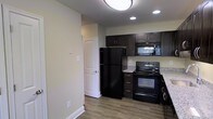 Located at 70 Old Dublin Pike in Doylestown, PA, this two-floor space offers a functional and contemporary layout designed with everyday comfort in mind. The kitchen is a standout feature, showcasing rich dark espresso-toned cabinetry that provides ample upper and lower storage. The countertops display a granite-look finish that pairs stylishly with the full suite of black appliances, including a full-size refrigerator, electric range, and over-the-range microwave. Recessed lighting alongside a flush-mount ceiling fixture ensures the kitchen is well-lit, creating a bright and practical cooking environment. The flooring throughout is a warm hardwood-style laminate that adds a cohesive, clean aesthetic to the space. Neutral, light-toned walls enhance the overall brightness and offer versatility for a variety of interior styles. A paneled interior door leads to an adjacent room, suggesting a thoughtful flow between living areas. The space is spread across two floors, offering separation between living and other functional zones. Overall, the design balances modern finishes with practical functionality, making it a well-appointed space in the heart of Doylestown.
