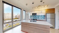 Located at 180 High Park Lane in Silver Spring, MD, this modern 2-bedroom, 2-bathroom residence offers a thoughtfully designed layout with clean, contemporary finishes throughout. Light hardwood-style flooring flows through the open living areas, complemented by bright white walls and abundant natural light streaming through expansive floor-to-ceiling windows that frame sweeping views of the Silver Spring skyline and surrounding treetops.

The open kitchen and living area serves as the heart of the home, featuring a sleek kitchen island with a white quartz countertop, wood-grain cabinetry, stainless steel appliances, a mosaic tile backsplash in cool blue and grey tones, and modern pendant lighting. Track lighting adds a refined, contemporary touch overhead.

Both bedrooms are generously sized, each with floor-to-ceiling windows offering elevated city and nature views, and access to closet space. The primary bedroom includes a private door to the balcony, enhancing its connection to the outdoors.

The two bathrooms are finished with wood-look tile flooring, dark-toned vanities with white countertops, and clean subway tile surround in the tub and shower areas. A smart thermostat is also present in the hallway, adding a modern convenience. Four closets throughout the unit provide ample storage for everyday living.