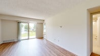 This single-floor unit offers a clean, functional layout designed for comfortable everyday living. The main living area is bright and open, featuring light wood-style vinyl flooring, crisp white walls, and a textured ceiling. A full-width sliding glass door floods the space with natural light and provides direct views of a lush green outdoor area with a decorative fountain, creating a tranquil backdrop. A second window in an adjacent room further enhances the sense of openness.

The kitchen is well-appointed with warm honey-toned wood cabinetry extending to the upper and lower walls, dark granite-style countertops, a double basin sink, and white appliances including a range and refrigerator. A notable convenience is the in-unit washer and dryer, seamlessly integrated within the kitchen space. Tile flooring in the kitchen provides a practical and easy-to-maintain surface.

The bedroom is generously proportioned with the same light wood-style flooring, ample closet space, and a window that allows in natural light. The bathroom features a full soaking tub and shower combination with tile flooring, maintaining the unit's clean and neutral aesthetic throughout. The overall ambiance is fresh, bright, and move-in ready.