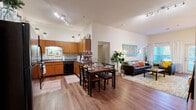 Located at 807 S Main St in Normal, IL, this single-floor unit offers a thoughtfully designed open-concept layout that seamlessly connects the kitchen, dining, and living areas. Rich hardwood flooring flows throughout the main living space, complemented by soaring ceilings that lend an airy, expansive feel.

The kitchen is well-equipped with warm wood cabinetry, granite-style countertops, black appliances including a refrigerator, range, and dishwasher, and a generous U-shaped layout providing ample counter and storage space. Pendant and track lighting add both function and style overhead.

The dining area accommodates a full table and flows naturally into the living room, which features tall ceilings, large windows with sheer curtains, and a glass door offering natural light and outdoor access. The bedrooms are comfortably sized with carpeted floors, large windows, and room for study or workspace setups.

The bathrooms are finished with wood-toned cabinetry, granite-style vanity tops, large mirrors, and hardwood-style flooring, maintaining a consistent, cohesive aesthetic throughout the unit. The overall design balances practicality with warmth, making this a comfortable and functional living space in Normal, IL.