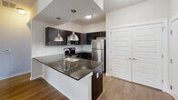 Located in Philadelphia's Roxborough neighborhood, this one-bedroom, one-bathroom residence offers a well-designed, efficient layout across a single floor. The open-concept kitchen and living area serves as the heart of the home, anchored by a peninsula with striking dark granite countertops, an undermount sink, and stylish pendant lighting. The kitchen is equipped with rich espresso-toned cabinetry, a glass tile backsplash, stainless steel appliances including a refrigerator and electric range, and ample storage. The living area extends naturally from the kitchen, featuring warm hardwood-style flooring and a glass-paneled door that invites natural light and provides outdoor access. The bedroom is a comfortable, carpeted retreat with a window that brings in additional natural light, and is accompanied by a dedicated closet. The full bathroom includes a soaking tub and shower combination, tile flooring, a dark-cabineted vanity with a white countertop, and clean, neutral finishes throughout. A hallway connects the main living spaces to the private areas of the home. The consistent use of neutral tones, modern fixtures, and quality materials gives the entire residence a cohesive, contemporary feel.
