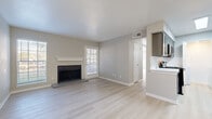 This single-floor residence offers a clean, modern aesthetic defined by light hardwood-style flooring, neutral warm-gray walls, and crisp white trim throughout. The open living area serves as the centerpiece of the home, highlighted by a classic wood-burning fireplace with a white mantel and tiled hearth. Natural light pours in through multiple windows fitted with plantation shutters, and a glass-paneled door provides direct outdoor access, enhancing the room's airy feel. A ceiling fan overhead adds to the comfort of the space.

The kitchen is thoughtfully designed with gray shaker-style cabinetry accented by gold hardware, white quartz countertops, and a white subway tile backsplash. It connects seamlessly to the living area via a pass-through counter. Conveniently tucked adjacent to the kitchen is an in-unit laundry area, offering practical day-to-day functionality.

The bedroom is generously sized, bathed in natural light from large windows, and features a ceiling fan along with a closet. The bathroom is well-organized, presenting a gray vanity with a white countertop, a bathtub-shower combination, and modern brushed-metal fixtures. The entryway is welcoming and functional, with a dedicated overhead light and direct access through a secure front door.