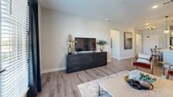 Located at 950 Jordan Creek Parkway in West Des Moines, Iowa, this well-appointed one-bedroom, one-bathroom residence offers a cohesive, modern design throughout its efficiently utilized single-floor layout. The open-concept kitchen and living area forms the heart of the home, anchored by a large center island with a quartz countertop, bar seating, and a deep undermount sink. White shaker cabinetry extends to the ceiling, complemented by stainless steel appliances, globe pendant lighting, and a built-in desk with wine rack storage — a functional and stylish touch. Wood-look flooring flows through the main living areas, lending warmth and continuity. The living room is bright and inviting, benefiting from natural light through windowed treatments and offering comfortable, open space for relaxing or entertaining. The bedroom features plush carpeting, generous natural light from dual windows, and a serene, neutral palette. The bathroom is finished to a high standard, showcasing a walk-in glass-enclosed shower with large-format tile, a white vanity with quartz countertop, and matte black hardware throughout. A dedicated in-unit laundry room with full-size washer and dryer and built-in shelving adds exceptional everyday convenience. Hallways connect each space seamlessly, creating a fluid, well-organized floor plan.